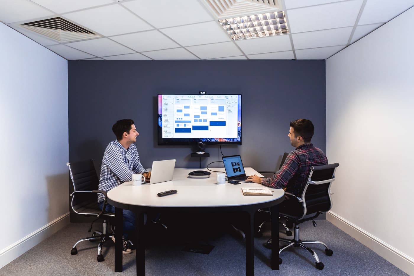 Two people in a meeting room reviewing a product wireframe on a wall-mounted screen