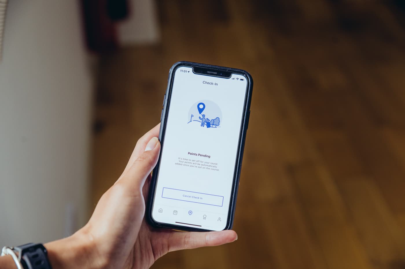 A hand holding a phone displaying a check-in screen from a live mobile app