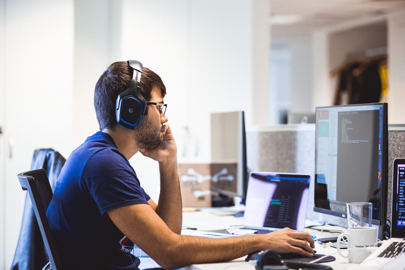 A developer with headphones working at a multi-monitor setup running a code editor